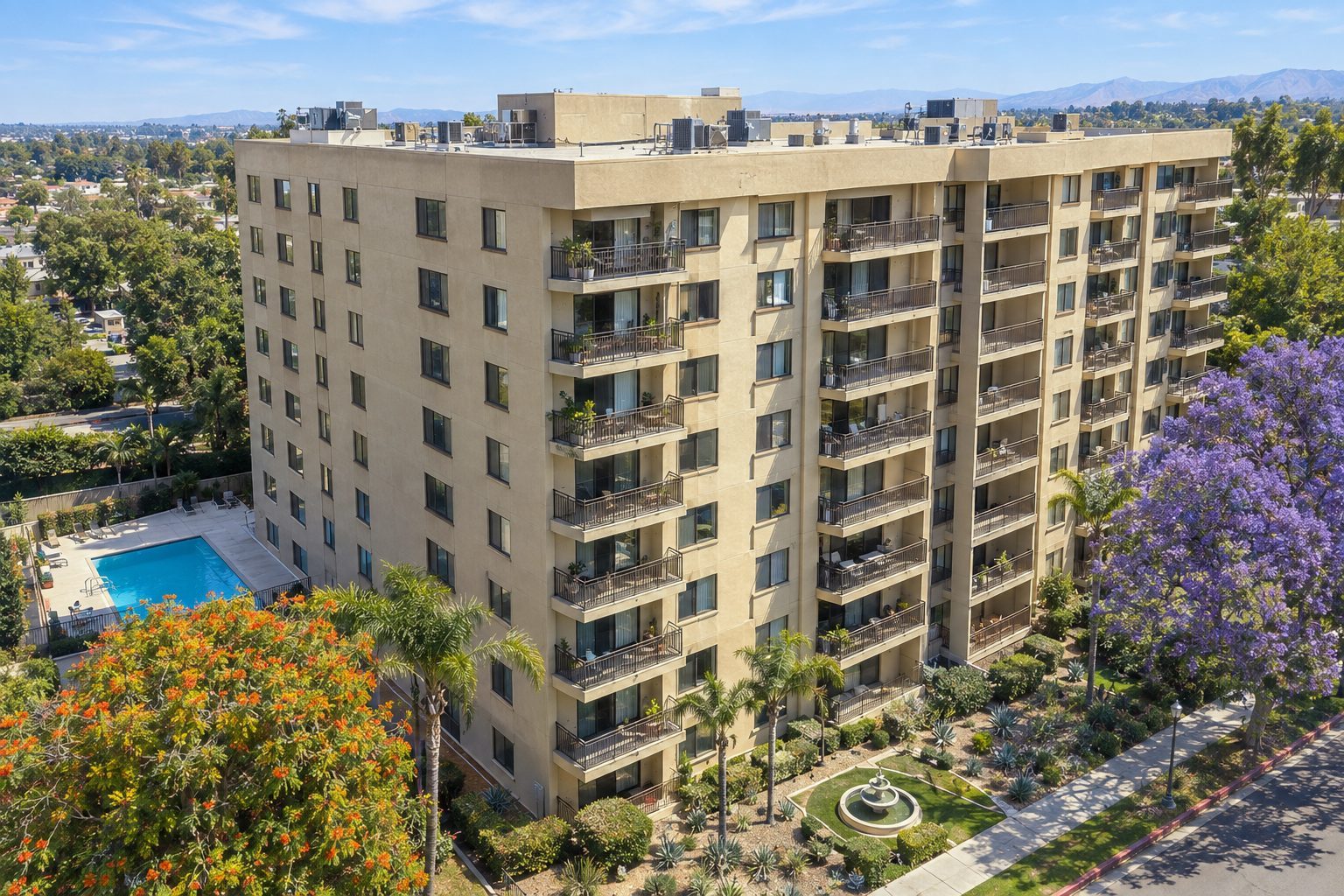 Aerial view of a nine-story condominium building with balconies, a pool and landscaped grounds